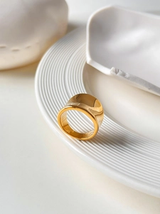 Detailed close-up of a wide polished 18K gold-plated titanium ring on white ceramic