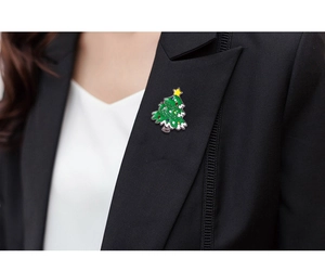 Detail shot of a green enamel Christmas tree brooch pinned on a black blazer lapel