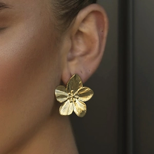 Matte vintage gold flower stud earrings in stainless steel shown on a model
