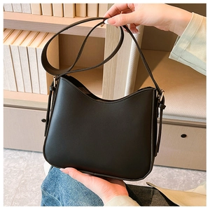 Détail d'un sac à bandoulière en cuir PU noir avec large sangle devant une étagère