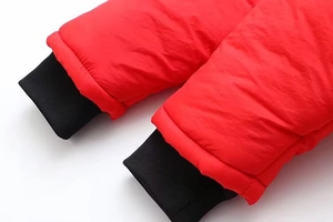 Détail du tissu en nylon rouge coupe-vent et poignets élastiques noirs sur la doudoune
