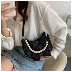 Detail of black satin shoulder bag featuring a large bow and elegant pearl chain handle