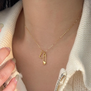 Close-up of gold heart safety pin necklace with letter L pendant on model