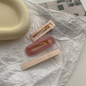 Detailed close-up of marble pink and cream matte hair clips with gold metal base
