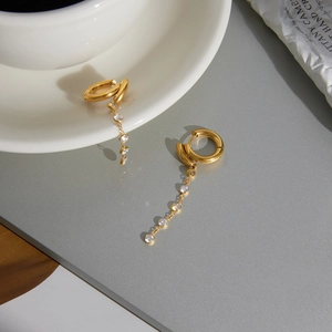 Détail de boucles d'oreilles à pampilles dorées avec oxydes de zirconium sur fond gris