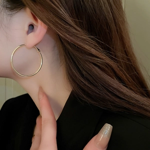 Close-up of a model wearing minimalist large round golden hoop earrings in polished metal