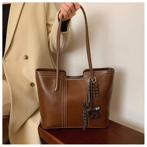 Close-up of brown leather tote bag with contrast stitching and decorative charms
