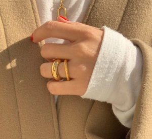Close-up of elegant gold dome and wavy rings on model's hand over autumn coat