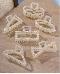 Detail view of 6 assorted pearl hair claw clips on a natural wood surface