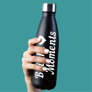 Détail d'une main tenant une gourde isotherme noire avec lettrage blanc artistique