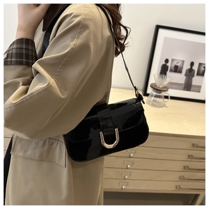 Close-up of black patent leather shoulder bag with gold horseshoe buckle on model