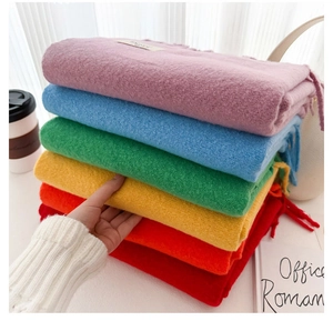 Close-up of soft knit scarves in multiple colors stacked on a cozy white desk setup