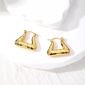 Macro detail of gold geometric triangle hoop earrings with vintage engraved textures