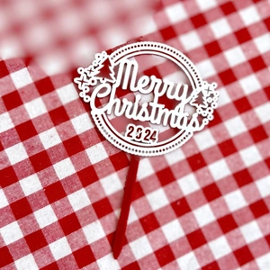 Macro shot of a white acrylic Merry Christmas 2024 cake topper with holiday tree details
