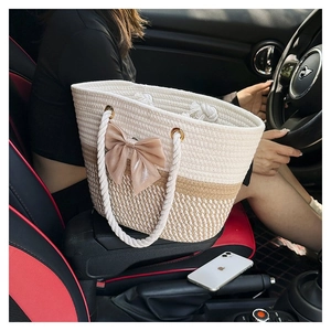 Detail of woven gradient tote bag with large beige bow accent on a car center console