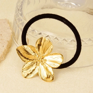 Black hair tie with a gold five-petal brushed metal flower on a minimal textured surface