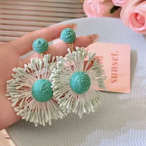Detail of mint green and blue raffia woven flower earrings with cotton tassels