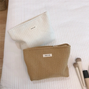 Textured boucle woven makeup bags shown in cream and camel with makeup accessories