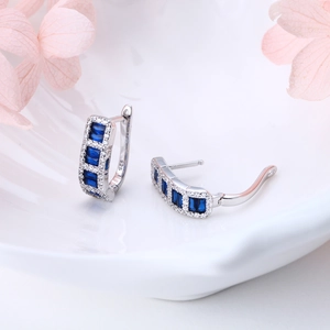 Macro shot of 925 silver earrings with blue square stones and white zircons on a white plate
