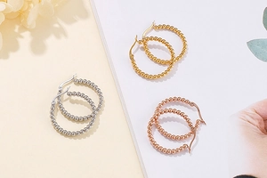 Detailed view of three pairs of beaded hoop earrings in gold, silver, and rose gold finishes