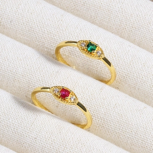 Detail of eye-shaped gold rings with emerald green and ruby red stones on beige fabric