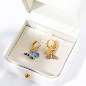 Détail de boucles d'oreilles créoles dorées avec papillons et diamants dans un écrin blanc