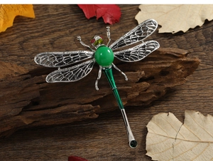Detail of silver dragonfly brooch with green stones on a rustic wood background