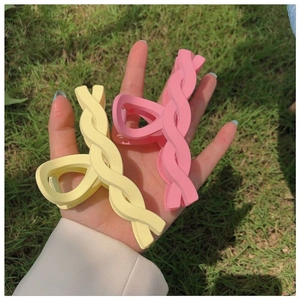 Close-up of matte pastel yellow and pink twisted hair claw clips held against grass