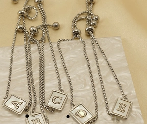 Detailed macro view of stainless steel letter pendants with white shell inlay and adjustable chain
