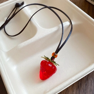 Close-up of translucent red strawberry pendant with green leaf and wax cord necklace
