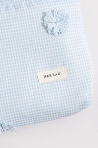 Close-up of light blue gingham fabric texture with 3D floral accent and brand label