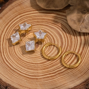 Detailed close-up of 18K gold-plated star and square stud earrings on wood