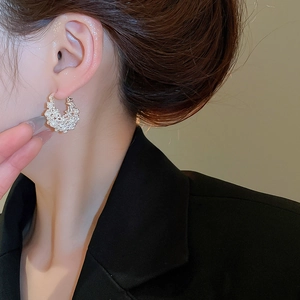 Detail view of C-shaped hoop earrings with micro-inlaid pearls and silver metal texture
