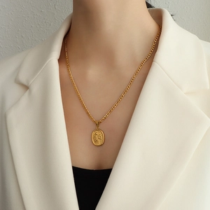 Golden titanium steel Figaro necklace with oval rose relief pendant on white suit model