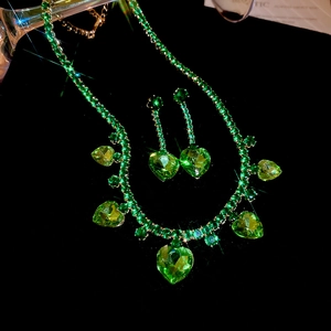 Detailed close-up of luxury gold necklace and earrings set with green heart gems