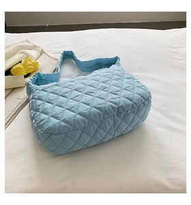 Detail shot of light blue quilted diamond bag on white bedding with yellow tulips