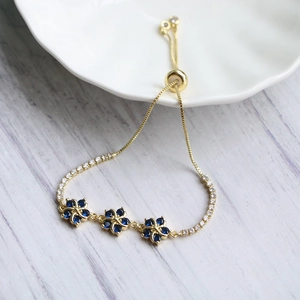 Detail eines verstellbaren Gold-Bolo-Armbands mit blauen Zirkon-Blumen und funkelnden Steinen