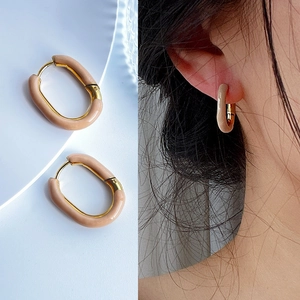 Detail view of gold U-shaped hoop earrings with cream enamel on a model and background