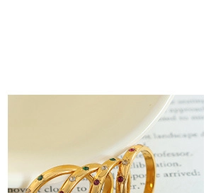Macro view of four thin gold rings with multicolor zircons on a white porcelain edge