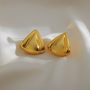 Macro shot of gold triangular stud earrings with mirror finish on white satin fabric