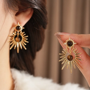 Detail of gold sunburst earring featuring tiger eye stone and zircon accents
