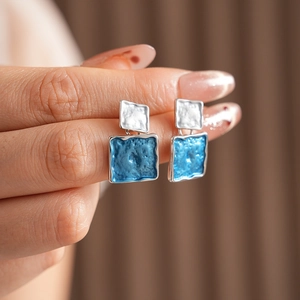 Macro detail of blue oil-drop square earrings with hammered silver metal texture