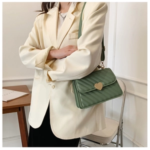 Detail of green pleated crossbody bag with gold heart clasp on beige blazer outfit