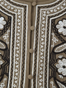Detailed embroidery with geometric flower patterns and cloth-covered buttons on linen top