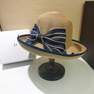 Elegant wide brim straw sun hat with dark blue ribbon bow on wooden stand