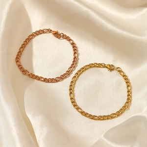 Gold and rose gold Figaro chain bracelets displayed on white silk fabric with lobster clasp