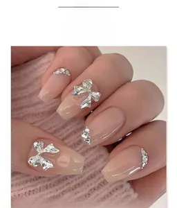 Macro detail of nude pink trapezoid press-on nails with silver bows and rhinestone accents
