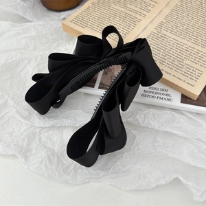 Close-up of black satin bow hair clips on white paper with vintage book props