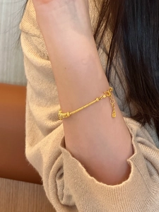 Close-up of a golden gourd bracelet with lock charm worn over beige knitwear