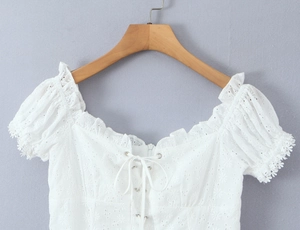 Close-up of white embroidery top featuring puff sleeves, square neck, and tie-front detail